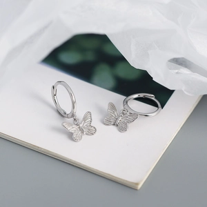 Detalle macro de pendientes de mariposa en plata con alas grabadas sobre fondo blanco