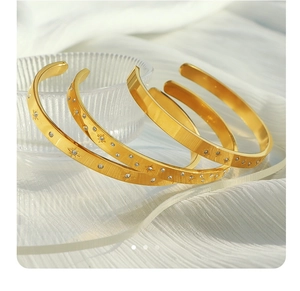 Detail of three-piece 18K gold plated zircon bangles on white silk fabric background