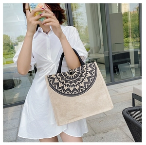 Ethnic style linen tote bag with black mandala print and woven handles in outdoor setting