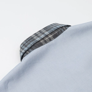 Détail du col de chemise bleu clair avec doublure à carreaux gris et bleu et coton