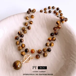 Tiger eye stone necklace with gold OT buckle displayed in a soft pink ceramic bowl