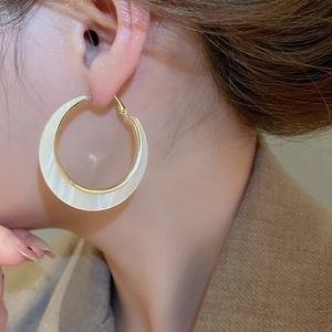 Dettaglio di un grande orecchino tondo dorato con inserto perlato bianco sulla modella