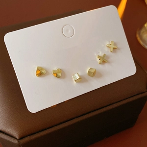 Close-up of three pairs of gold minimalist studs in heart, cube, and cross shapes