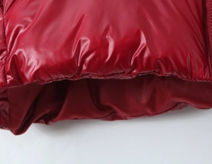 Close-up of red glossy puffer jacket hem showing detailed stitching and fabric texture
