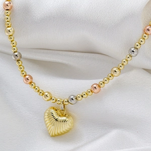 Detail of tri-color beaded necklace featuring a textured golden heart pendant on white silk