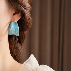 Close-up of blue marble resin hoop earring with gold post worn by a model