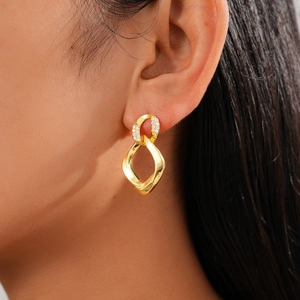 Close-up of gold twist earrings with shimmering zircon details worn by a model