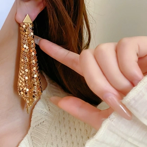 Close-up of long gold mesh tassel earrings with triangular studs on a fashion model