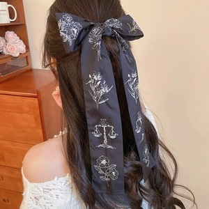 Detail of a black satin bow hair tie with white floral print on a long ribbon band