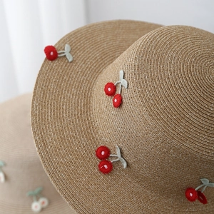 Close-up of straw sun hat featuring detailed 3D cherry embroidery and woven texture