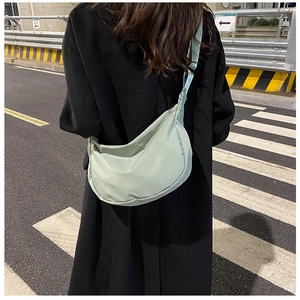 Detail of light green crescent nylon bag with adjustable strap worn on black coat