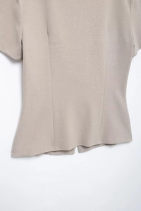 Detailed macro view of the light beige woven fabric texture and hemline of the short sleeve top