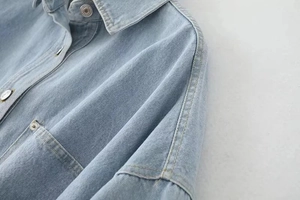 Detailed close-up of light blue denim shirt showing metallic button and reinforced stitching