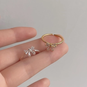 Detail of bow-shaped copper rings with pavé zircon in gold and silver finish