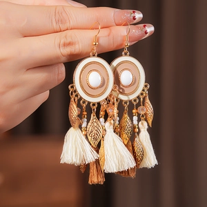 Macro shot of vintage gold earrings with beige tassels and metallic leaf pendants