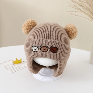 Détail du bonnet en tricot pour bébé avec trois ours brodés et deux pompons doux