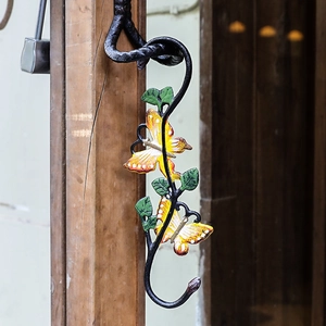 S-shaped cast iron hook with painted butterflies and green leaves on rustic wooden post
