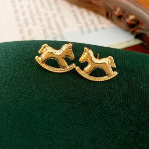Golden rocking horse stud earrings with hammered texture on dark green velvet