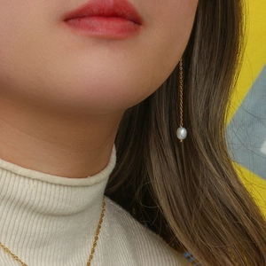 Dettaglio della collana a catena dorata e orecchini lunghi con perle indossati da modella