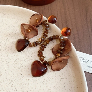 Detail of amber beaded hoop earring with heart pendant and mesh flower on ceramic tray