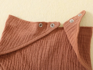 Detail of red-brown muslin baby bib fabric with high-quality metal snap buttons
