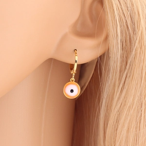 Close-up of gold evil eye earring with orange enamel charm worn by a model
