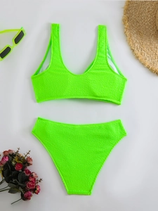 Flat lay of neon green bikini set with textured fabric, straw hat and sunglasses