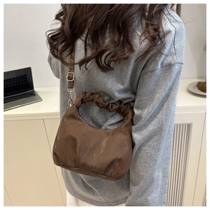 Model trägt dunkelbraune gefaltete Dumpling-Tasche mit eleganter Goldkette und Details
