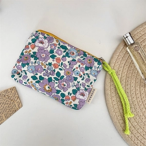 Detailed view of floral canvas makeup pouch with yellow zipper and green woven rope