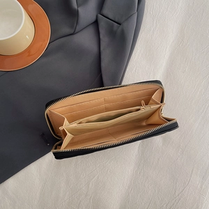 Black long zipper wallet with multi-card slots and gold hardware on grey suit background