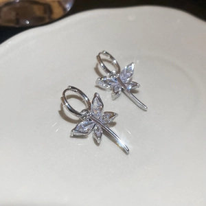 Macro shot of silver dragonfly earrings with sparkling zircons on a white plate