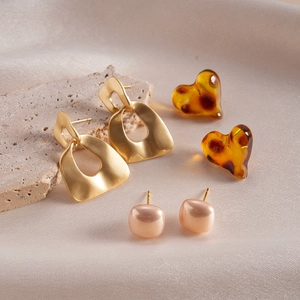 Close-up of geometric gold, amber heart and rose gold square resin stud earrings