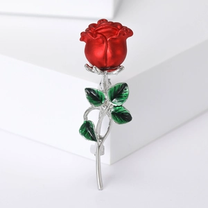 Macro detail of elegant red enamel rose brooch with green leaves on silver metal stem