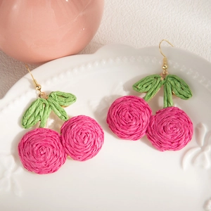 Macro shot of handmade woven cherry earrings with raffia texture and golden hooks