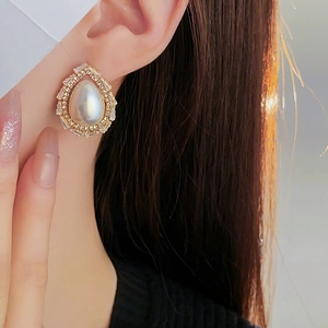 Close-up of elegant gold drop earrings with pearl and rectangular zircons on model