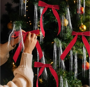 Detail of red velvet Christmas tree bow with silver tinsel hanging on decorated branches