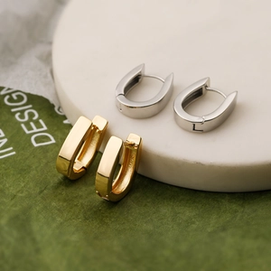 Minimalist U-shaped gold and silver earrings set displayed on white stone and leaf