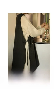 Detail of black cotton linen apron featuring golden Certain embroidery and side tie