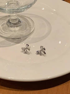 Detail shot of silver bow earrings with zircon stones on a white ceramic dish