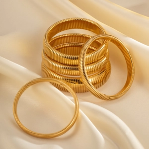 Set aus sechs goldenen Edelstahl-Spiralarmreifen auf luxuriösem weißem Satinhintergrund