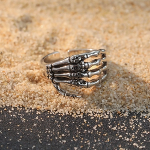 Retro punk skeleton claw open ring in vintage metal finish on dark sand background