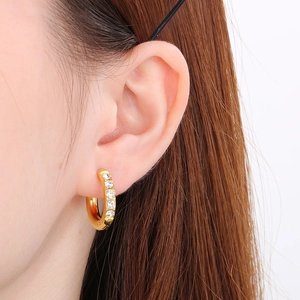 Close-up of gold U-shaped stainless steel earrings with sparkling zircon on earlobe