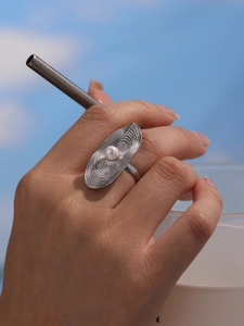 Detail of silver wavy ring with pearl inlay shown worn on finger against blue sky