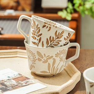 Hand-painted ceramic coffee mugs with brown floral motifs on a cream base, stacked neatly