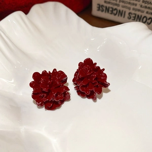 Detailed view of dark red floral stud earrings on a white decorative shell tray