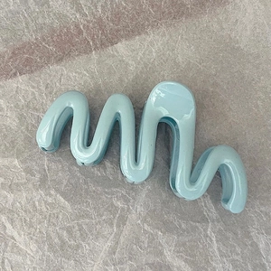 Detail showing wave-shaped blue hair claw clip with glossy jelly finish on textured paper