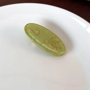 Close-up of green oval resin clip with gold foil flakes on white ceramic plate