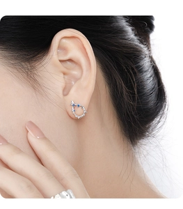 Detail of silver branch stud earring with blue gemstone worn by a fashion model