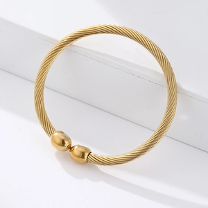 Macro detail of golden twisted cable bangle with smooth spherical ends on white podium