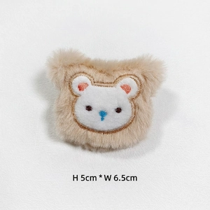 Detail of plush beige bear patch with blue nose and embroidery, 5cm by 6.5cm size